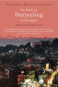 A book cover for "No Path in Darjeeling Is Straight: Memories of a Hill Town" by Parimal Bhattacharya. The cover features a vibrant aerial view of Darjeeling at night, with colorful buildings, illuminated signs, and bustling streets.