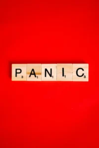  Scrabble tiles spelling out the word "PANIC" on a red background.